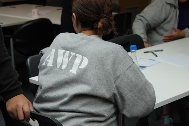 A woman in Arohata Women's Prison take part in Write Where You Are class. She is wearing a grey sweater with capital letters AWP on the back.