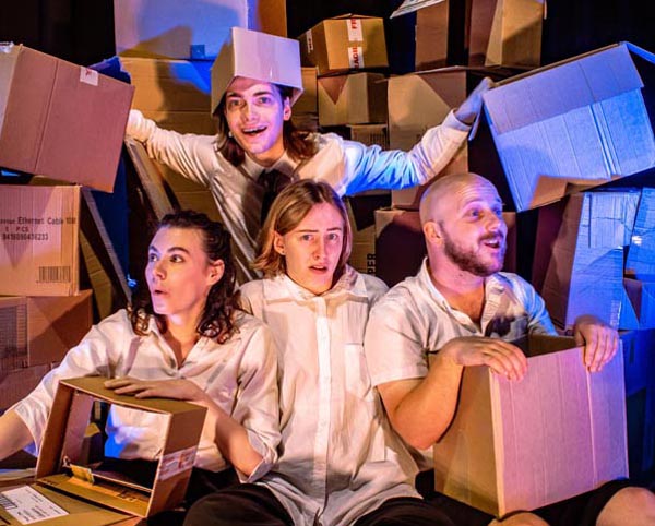 Four young performers sit on stage, surrounded by cardboard cartons