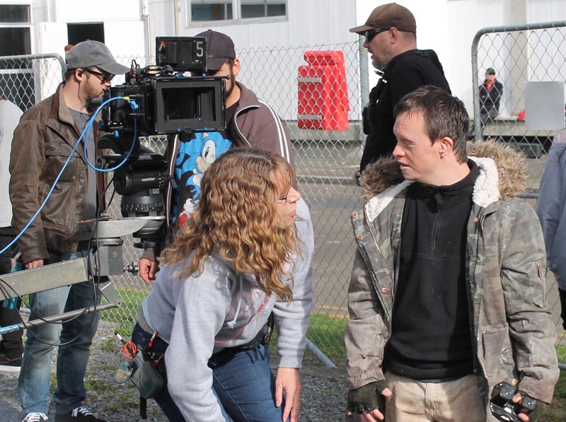 Duncan Armstrong is wearing a heavy jacket and talking to a woman with long curly hair. Behind them are three cameramen with a large camera.