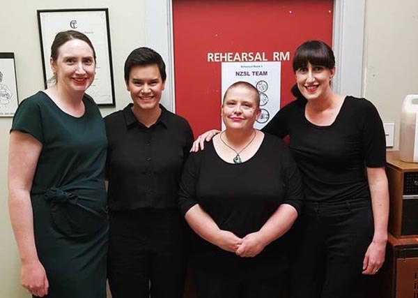 NZSL interpreters of the Cinderella pantomime stand in from of a red door and a sign that reads "NZSL TEAM". From left: Alisha Dimock, Angela Murray, Kellye Bensley and Melissa Sutton