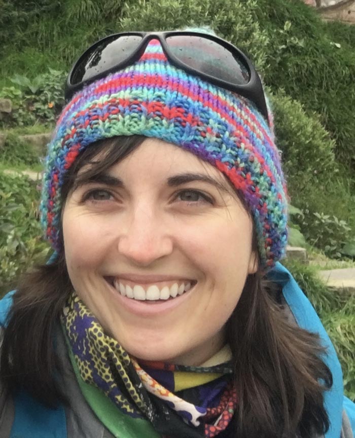 A portrait image of a smiling Katie Querin, wearing a colourful woolly hat  