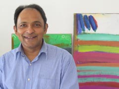 Portrait image of Dev Singh, standing alongside an artwork in Arts Access Aotearoa's office