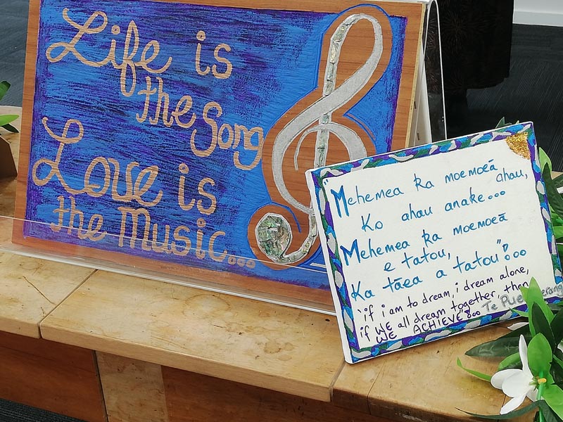 An artwork on display at a presentation of Home Ground's Project Toru. The artwork has a blue background with the text "Life is the song Love is the music" written in gold-coloured paint alongside a treble clef 