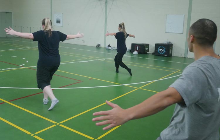 Kristie Mortimer teaches dance  to men in Rimutaka Prison. She is in a gymnasium, with a green floor