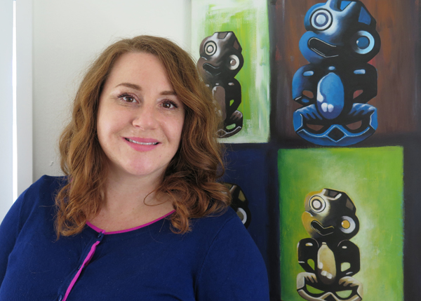 Portrait image of Dawa Devereux, standing alongside an artwork in Arts Access Aotearoa's office