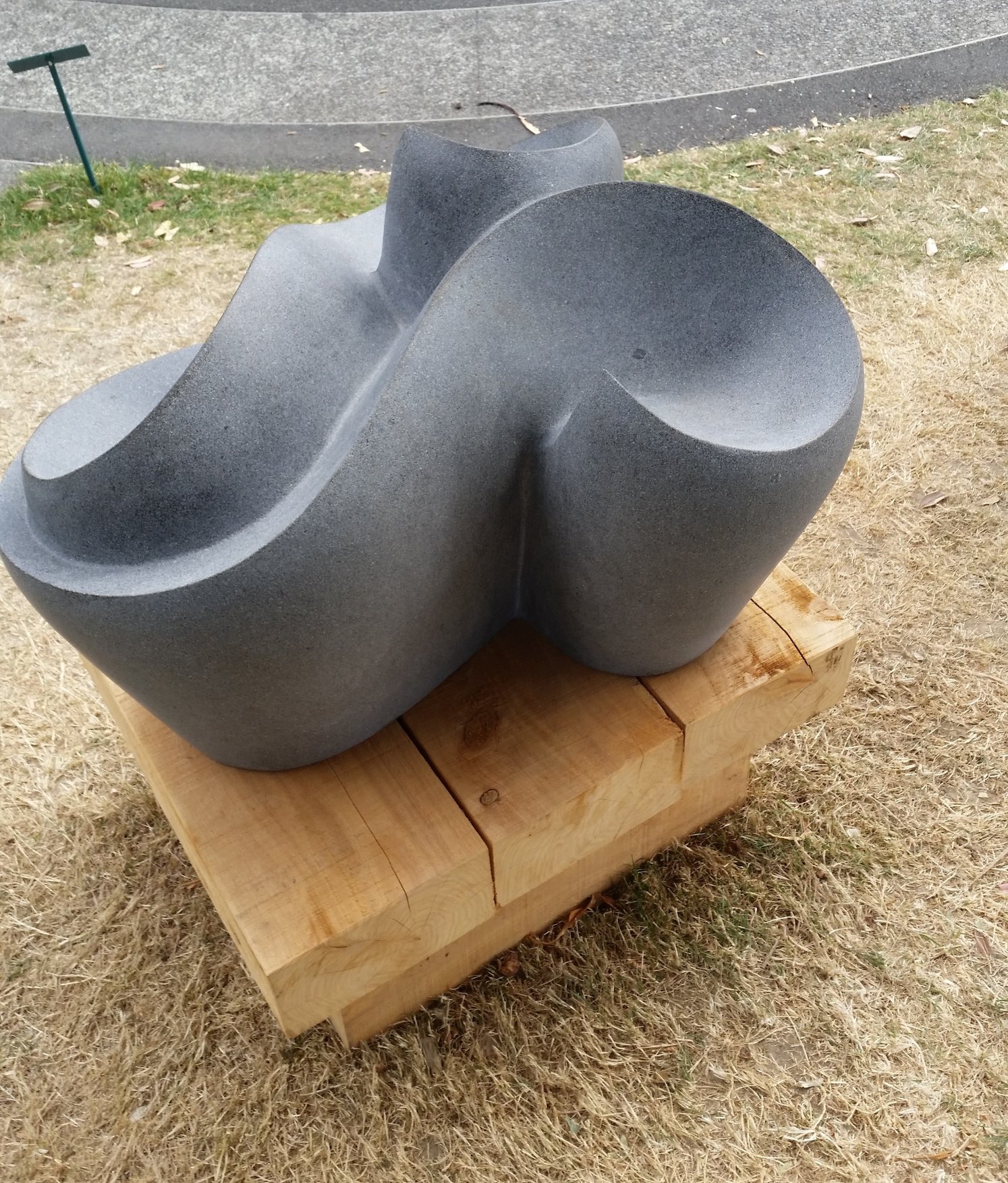 Claire Sadler's Us, a tactile, low, curved and multi-faceted stone sculpture on a rough sleeper base