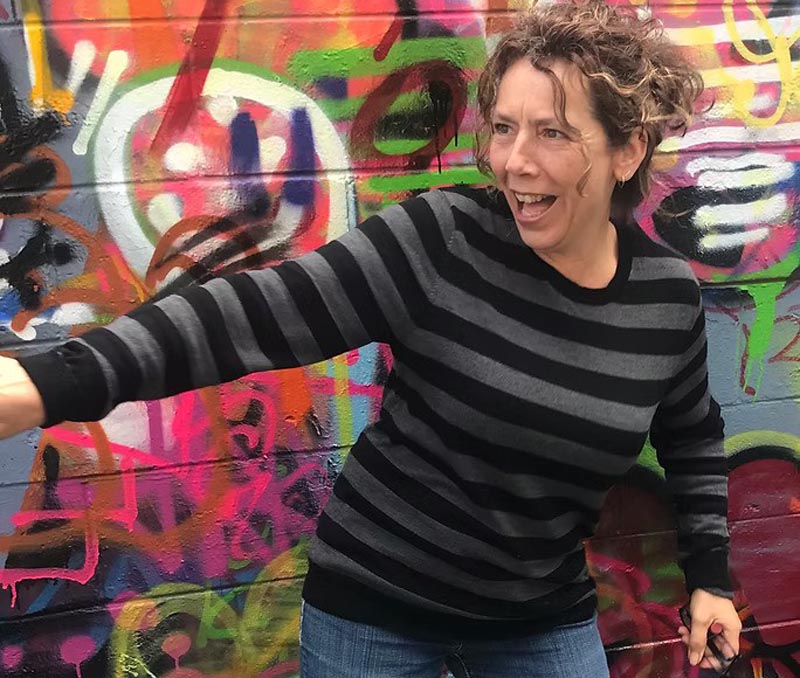 A close-up of youth worker Sarah in front of a colourfully painted wall