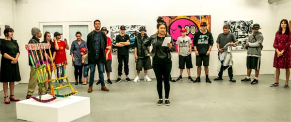 A young woman makes a speech, surrounded by Kākano artists and tutors