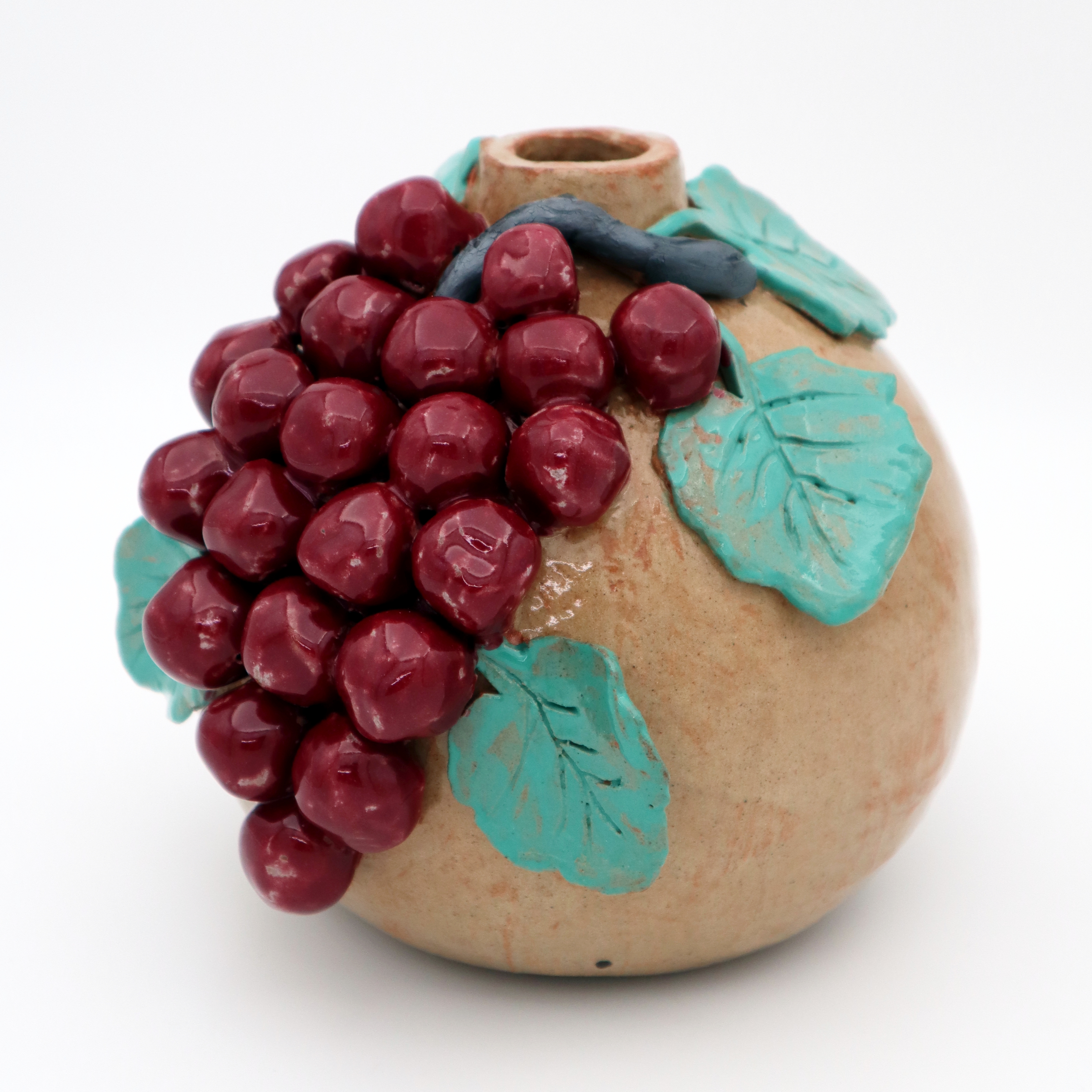 A round ceramic vase with three dimensional red grapes cascading down one side