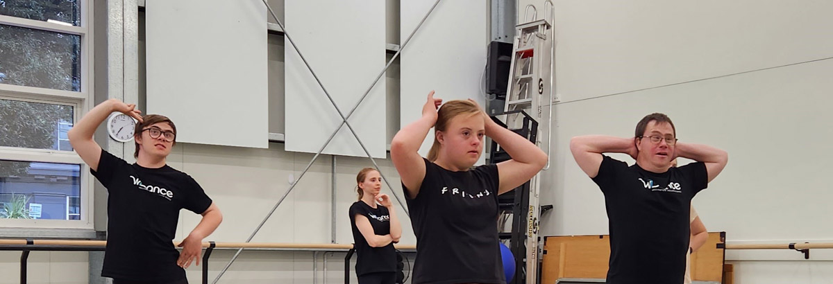 Four dancers wearing black pose in a dance studio.