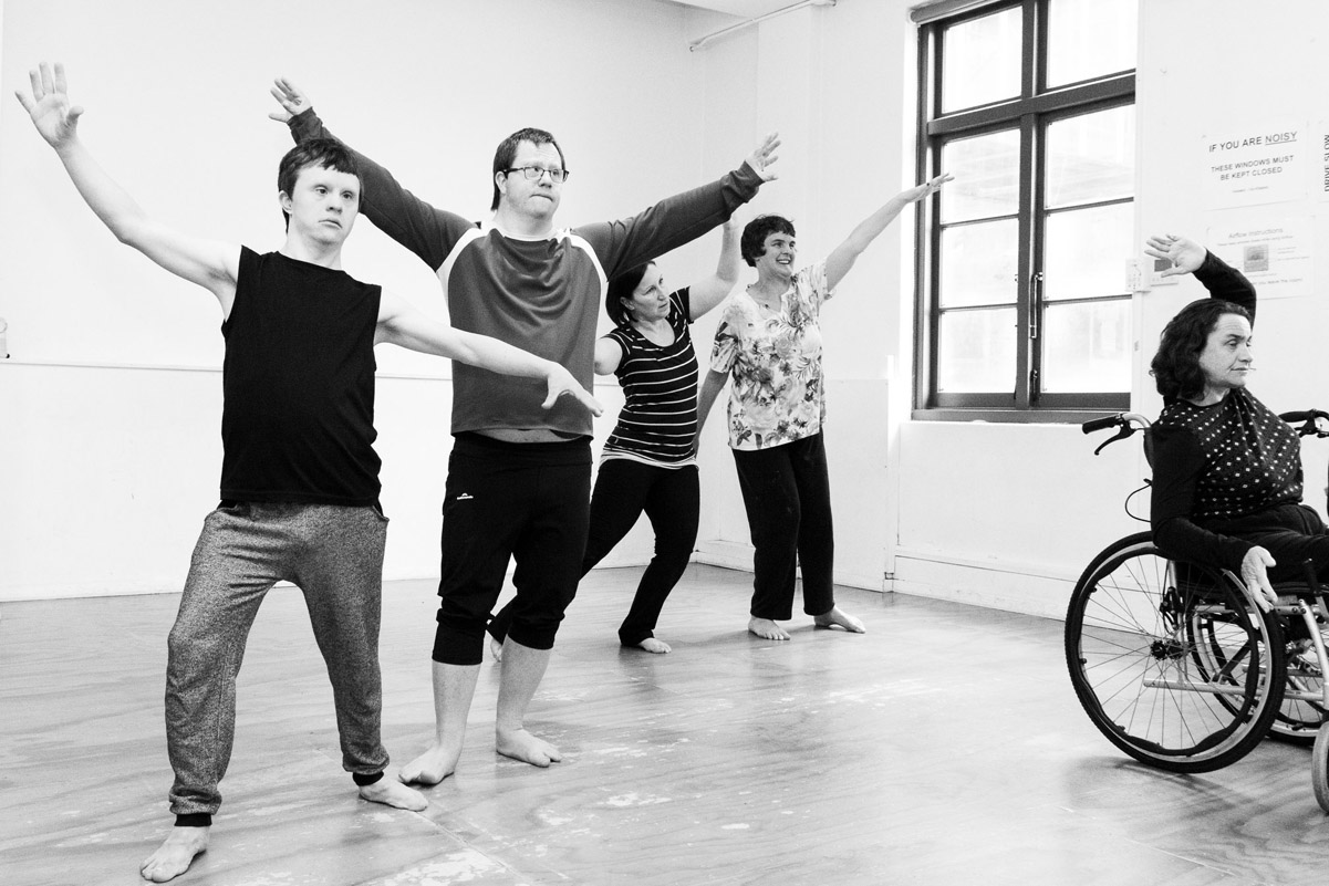 5 dancers in a small studio practice their moves, one in a wheelchair, four standing.